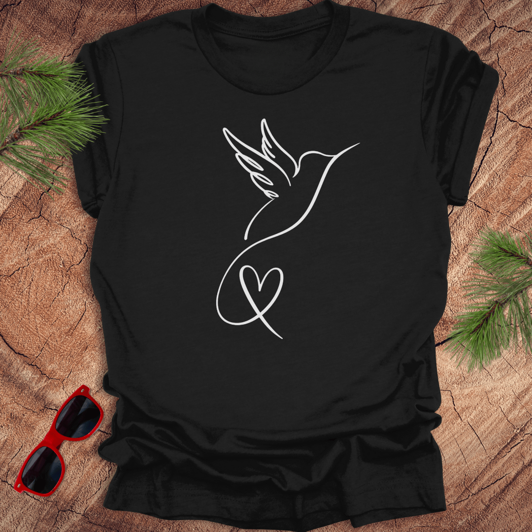 Black t-shirt with hummingbird and heart design on a wooden surface with sunglasses and greenery.
