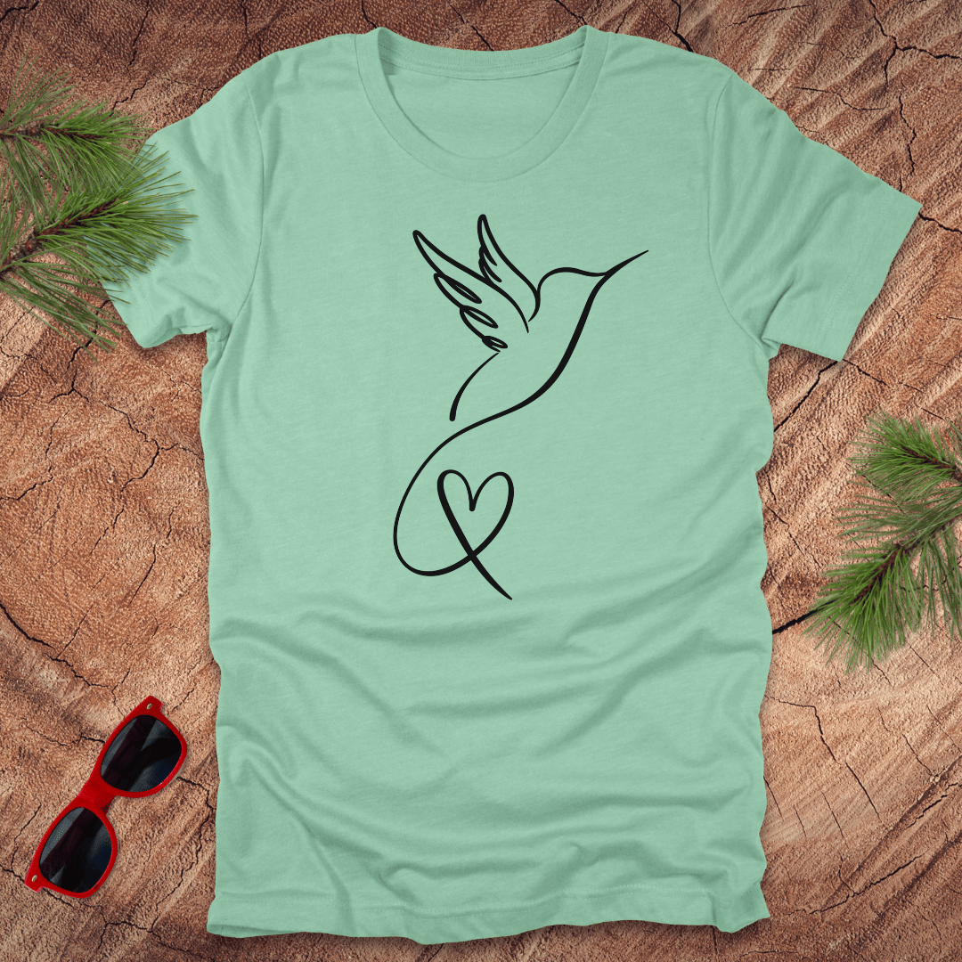 Mint green t-shirt with hummingbird and heart design on a wooden surface with sunglasses and greenery.