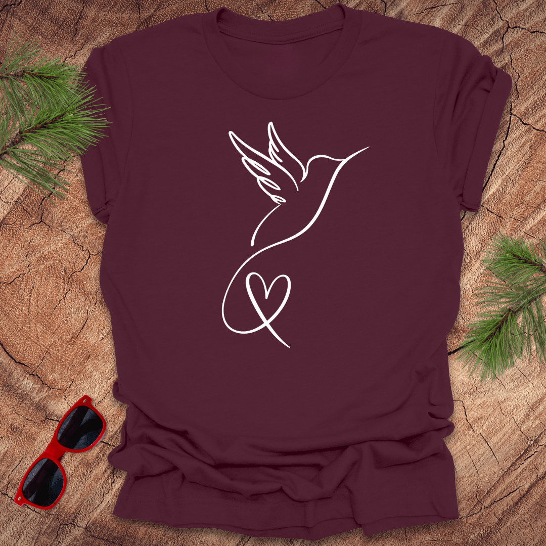 Maroon t-shirt with hummingbird and heart design on a wooden surface with sunglasses and greenery.