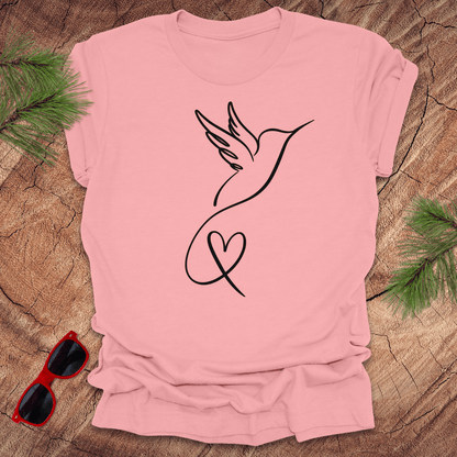 Pink t-shirt with hummingbird and heart design on a wooden surface with sunglasses and greenery.