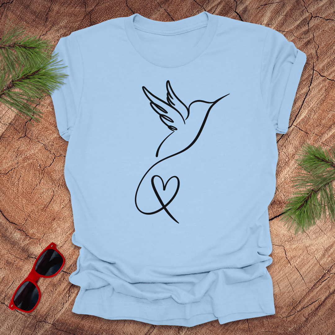 Baby blue t-shirt with hummingbird and heart design on a wooden surface with sunglasses and greenery.