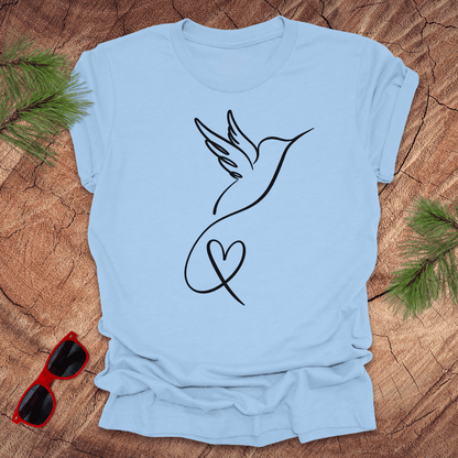 Baby blue t-shirt with hummingbird and heart design on a wooden surface with sunglasses and greenery.