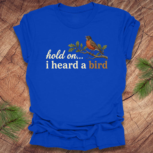 Royal blue t-shirt with a bird graphic and text 'hold on...i heard a bird' on a wooden background