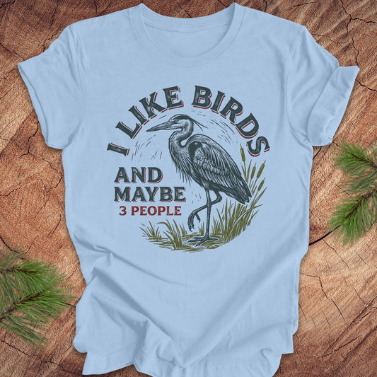 Light blue t-shirt with heron graphic and text, 'i like birds and maybe 3 people' on a wooden surface