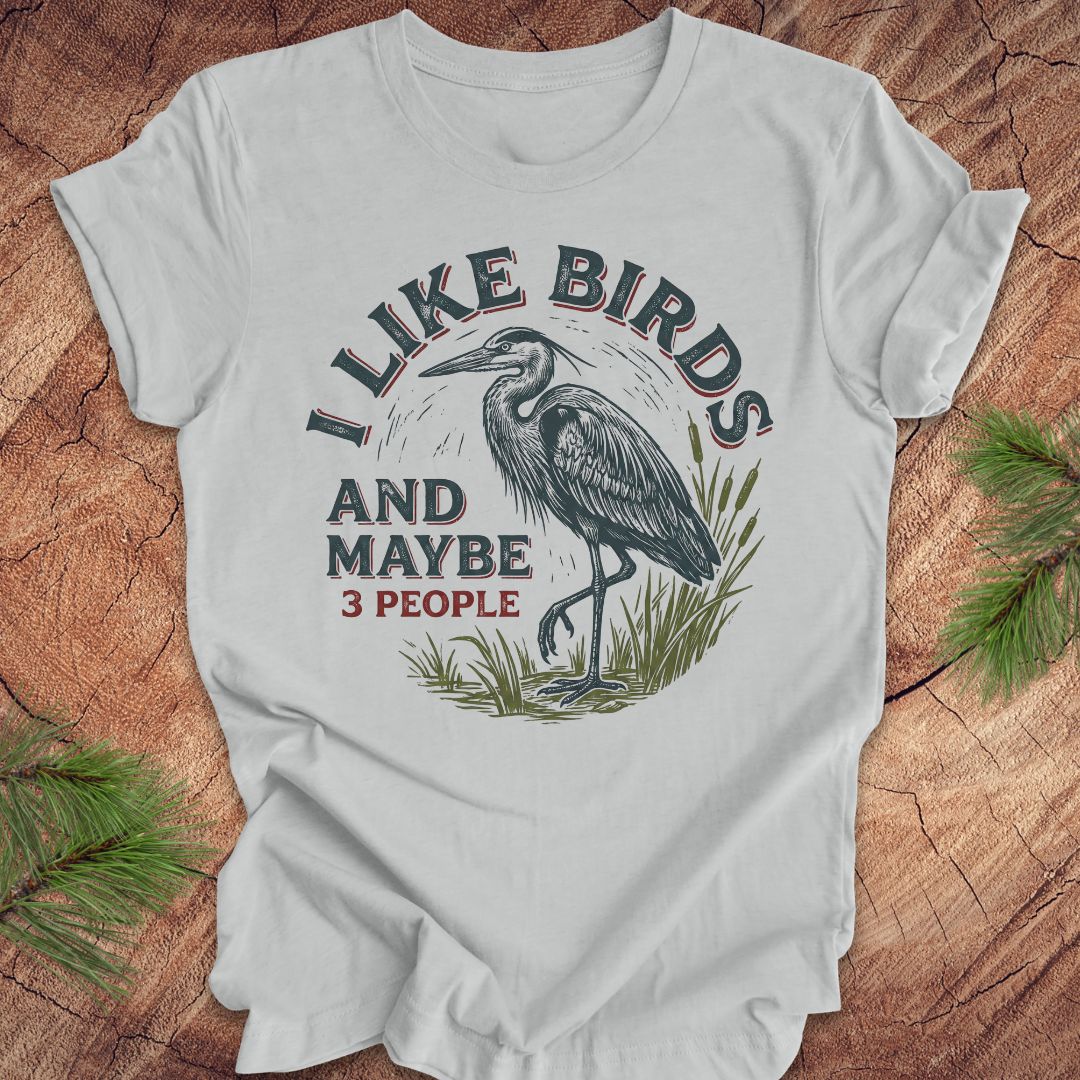 Gray t-shirt with heron graphic and text, 'i like birds and maybe 3 people' on a wooden surface