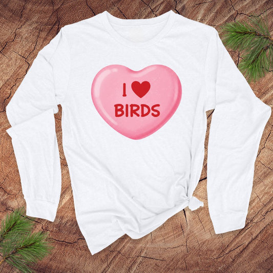White long-sleeve shirt with a pink heart-shaped candy graphic and 'I ❤️ BIRDS' text on a wooden surface.