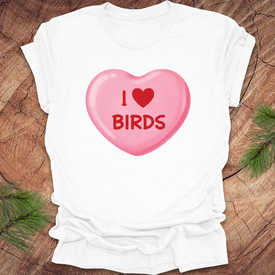 White t-shirt with a pink candy heart graphic and 'I ❤️ BIRDS' text on a wooden surface.