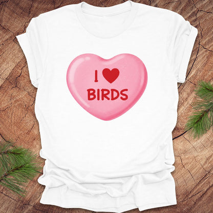 White t-shirt with a pink candy heart graphic and 'I ❤️ BIRDS' text on a wooden surface.