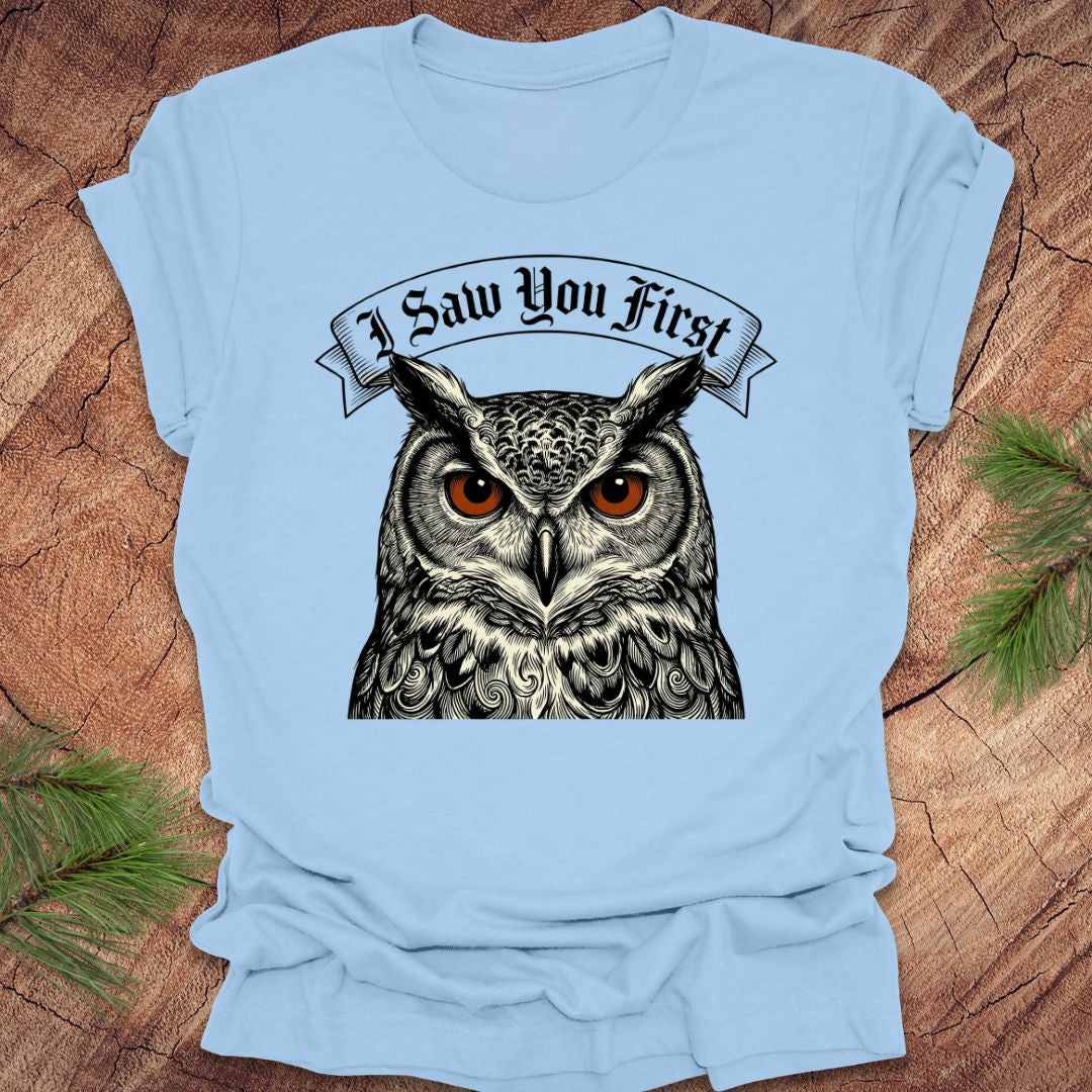 Light blue t-shirt with an owl graphic and text 'I Saw You First' on a wooden surface.