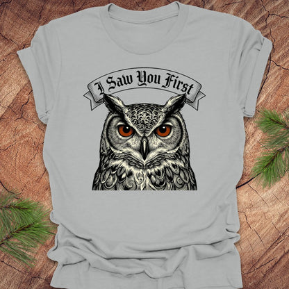 Gray t-shirt with an owl graphic and 'I Saw You First' text on a wooden surface.