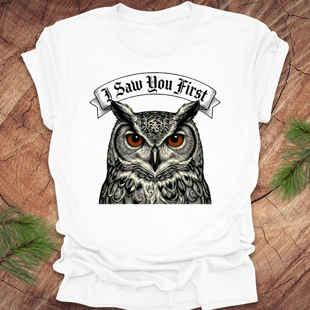 White t-shirt with an owl graphic and text 'I Saw You First' on a wooden surface.