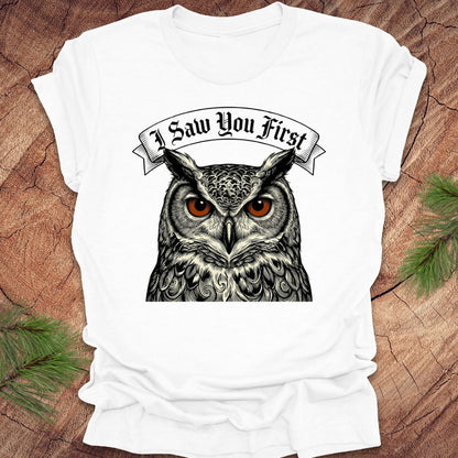 White t-shirt with an owl graphic and text 'I Saw You First' on a wooden surface.