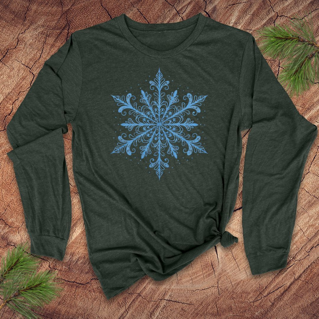 Green long-sleeve shirt with an icy blue snowflake design on a wooden surface with pine branches.