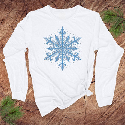 White long-sleeve shirt with an icy blue snowflake design on a wooden surface with pine branches.