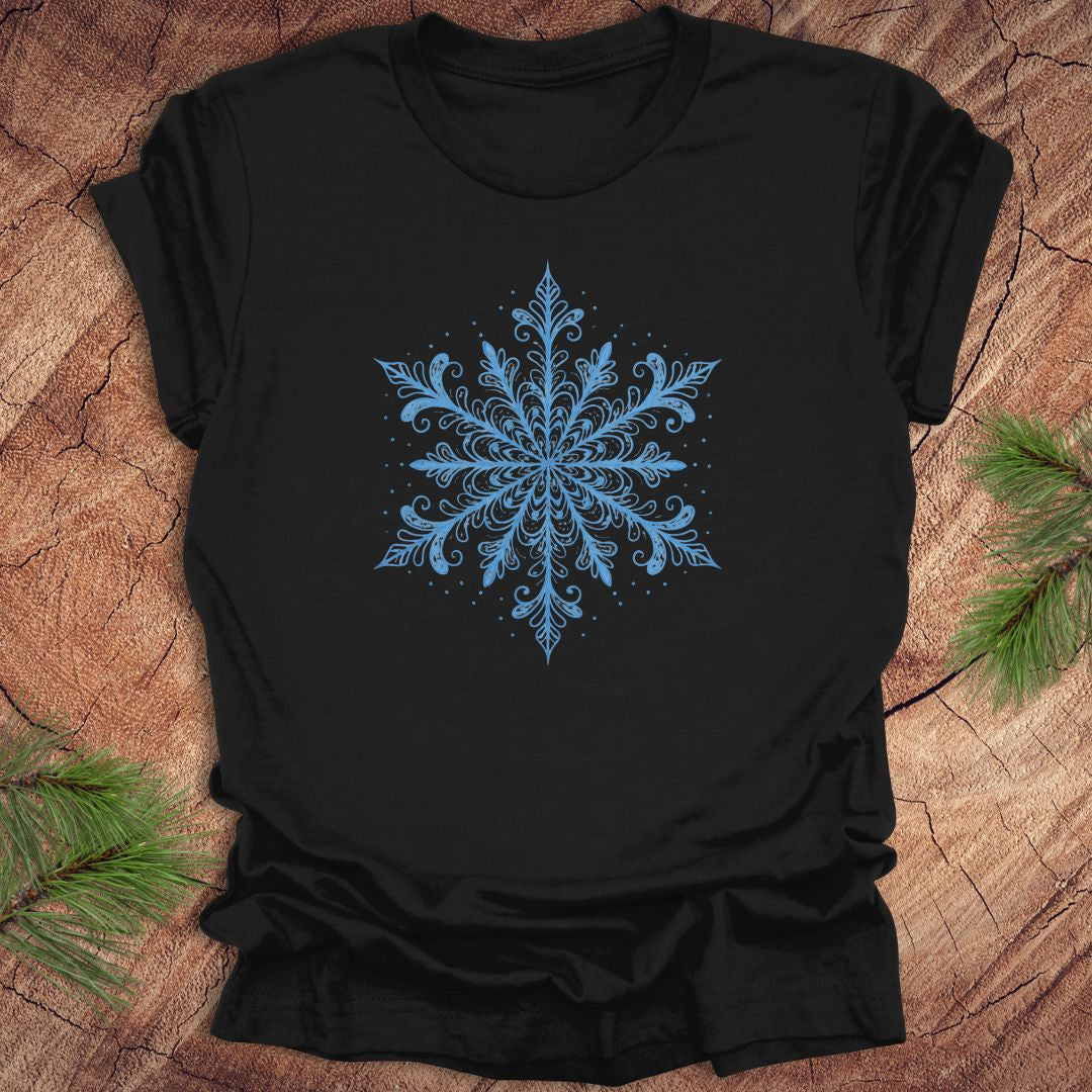 Black t-shirt with an icy blue snowflake design on a wooden surface with pine branches.