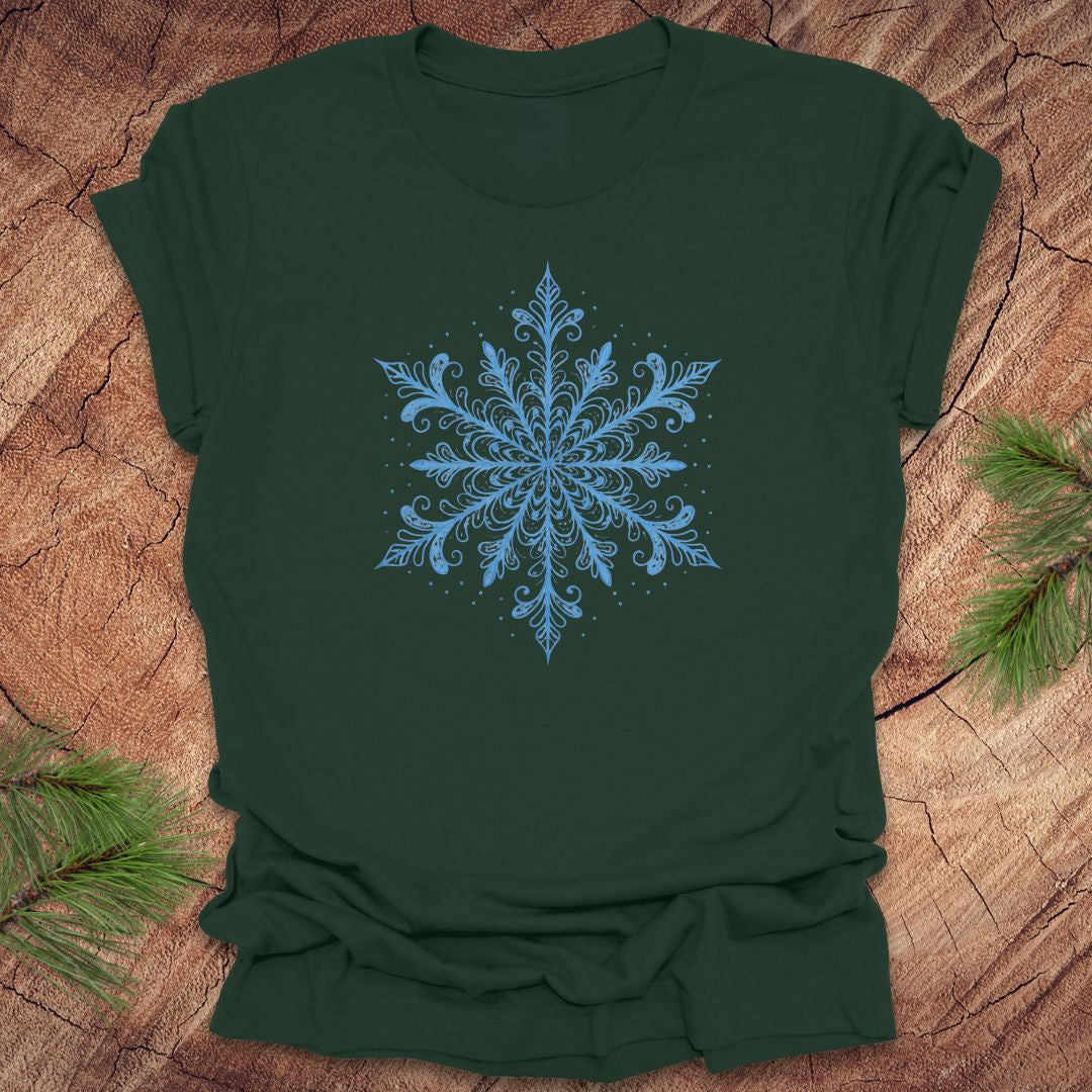 Green t-shirt with an icy blue snowflake design on a wooden surface with pine branches.