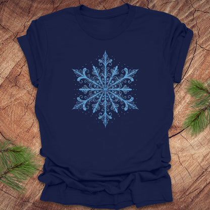 Navy blue t-shirt with an icy blue snowflake design on a wooden surface with pine branches.