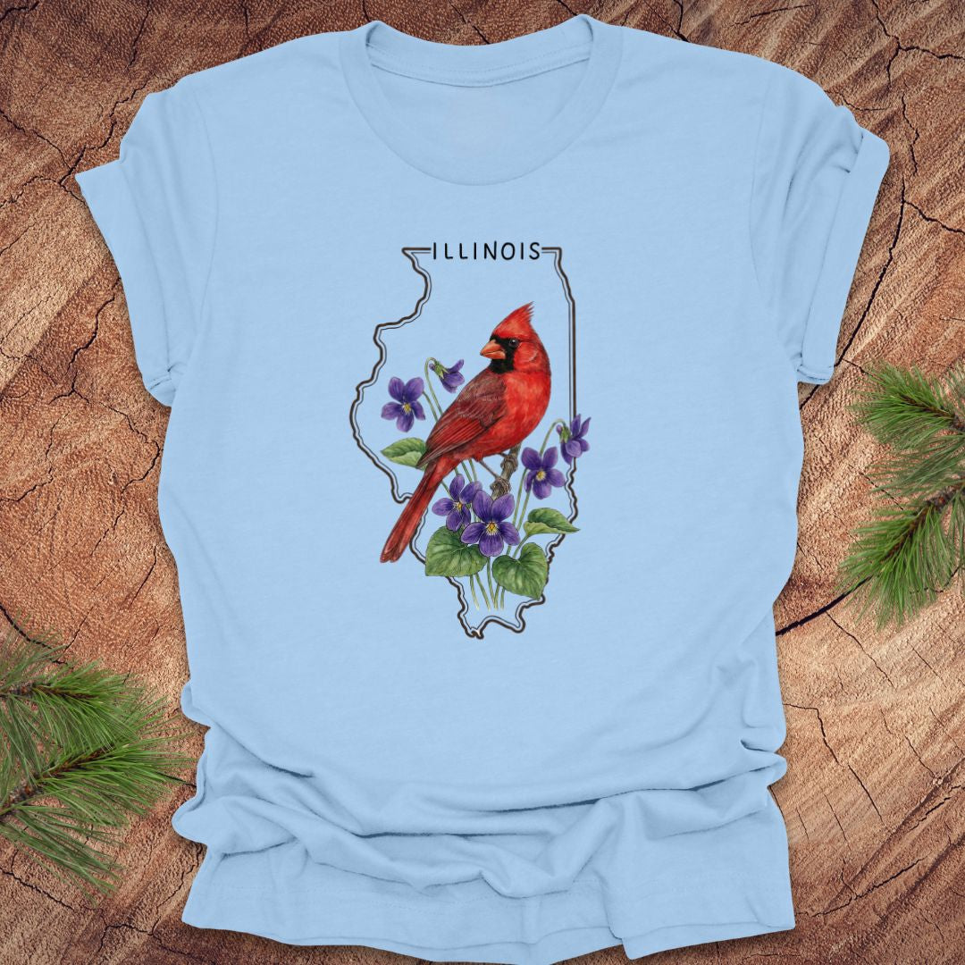 Baby blue t-shirt with Illinois state outline and state bird and flower cardinal and violets design on a wooden surface