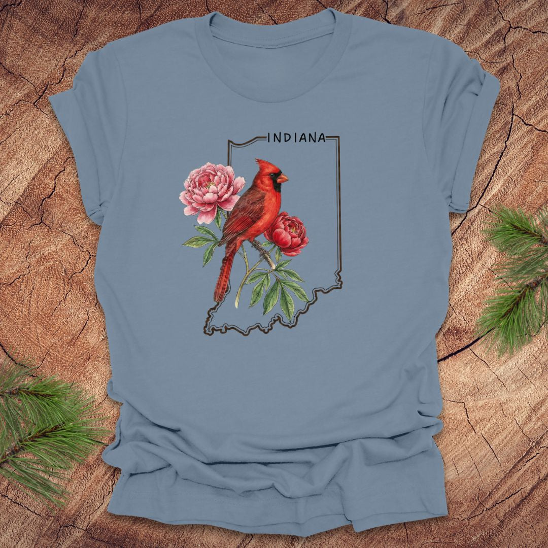 Steel blue t-shirt with a red cardinal and peony design on an outline of Indiana, placed on a wooden surface.