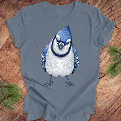 Blue t-shirt with a blue jay bird design on a wooden surface with pine branches.