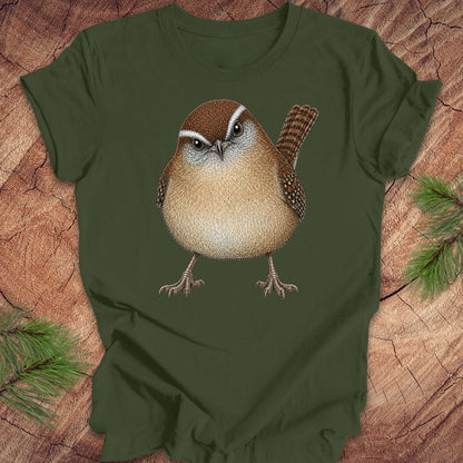 Green t-shirt with a carolina wren design on a wooden surface with pine branches.