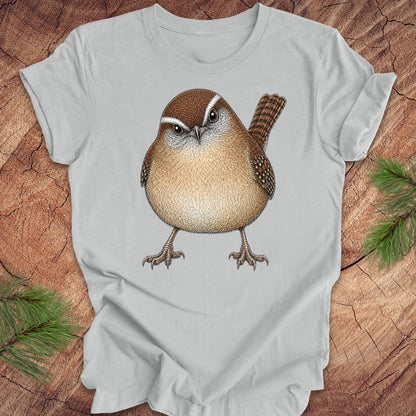 Gray t-shirt with a carolina wren design on a wooden surface with pine branches.