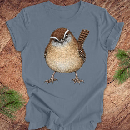 Blue t-shirt with a carolina wren design on a wooden surface with pine branches.