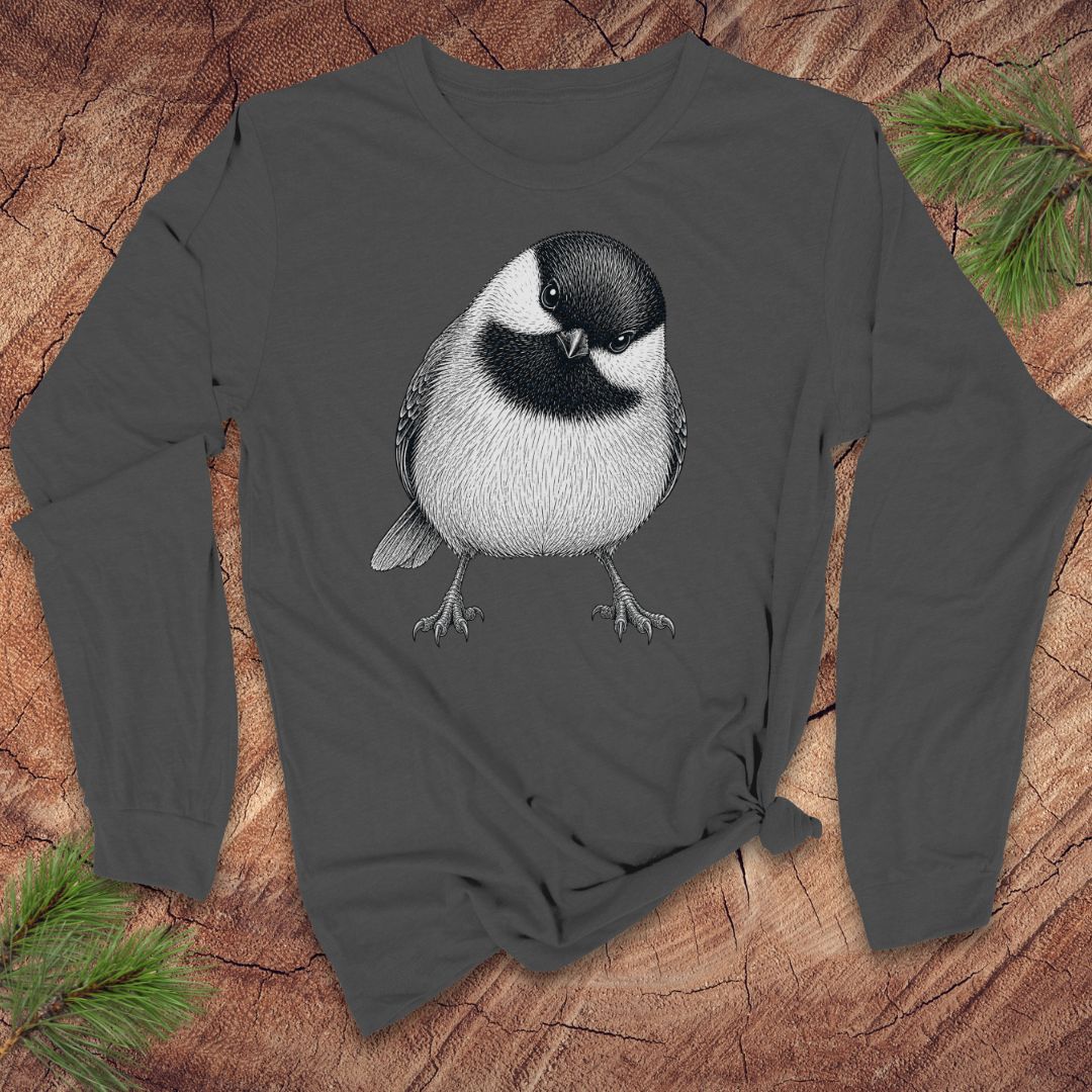 Dark gray long-sleeve shirt with a chickadee design on a wooden surface with pine branches.
