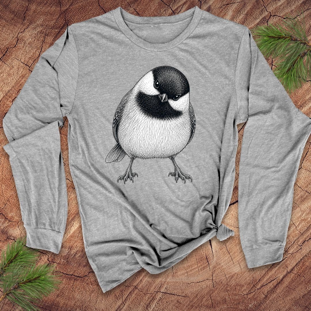 Gray long-sleeve shirt with a chickadee design on a wooden surface with pine branches.
