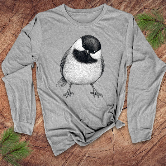 Gray long-sleeve shirt with a chickadee design on a wooden surface with pine branches.