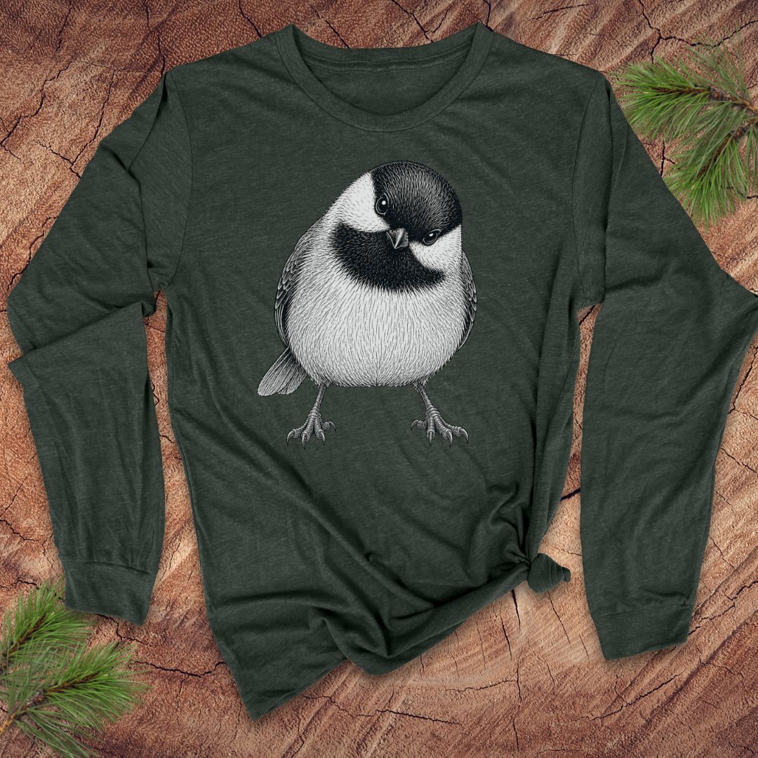 Green long-sleeve shirt with a chickadee design on a wooden surface with pine branches.
