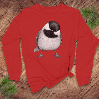 Red long-sleeve shirt with a chickadee design on a wooden surface with pine branches.