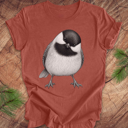 Rust colored t-shirt with a chickadee design on a wooden surface