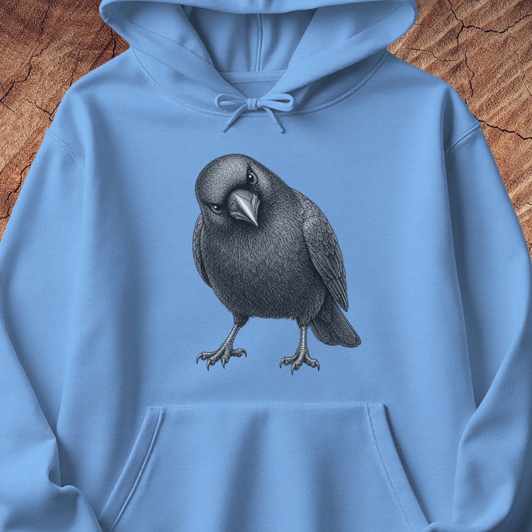 Carolina blue hoodie with a detailed pencil-style American Crow tilting its head and glaring, laid flat on a rustic wood background.