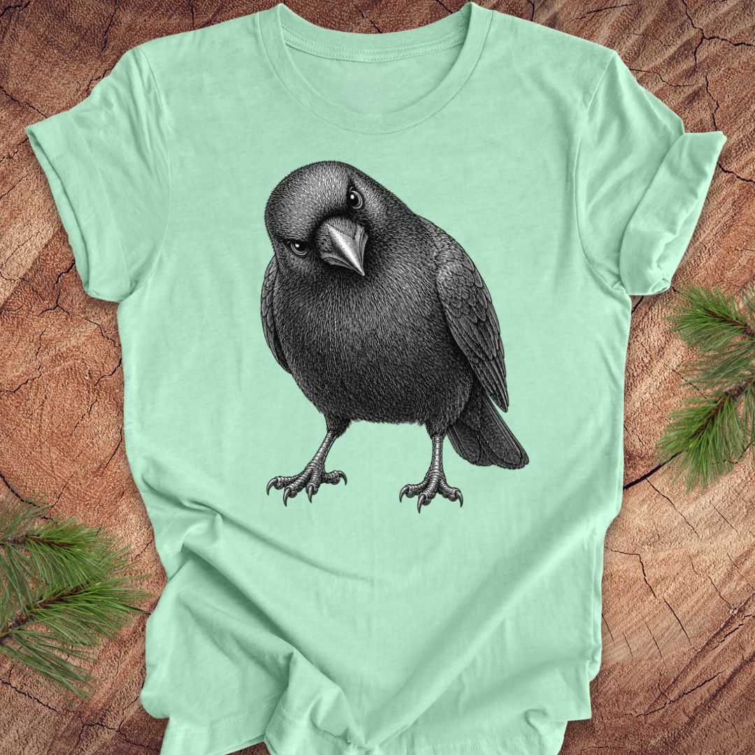 Mint green t-shirt with a crow design on a wood background.
