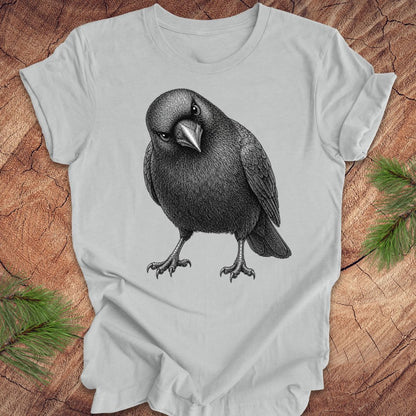 Gray t-shirt with a crow design on a wood background.