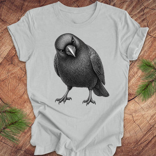 Gray t-shirt with a crow design on a wood background.