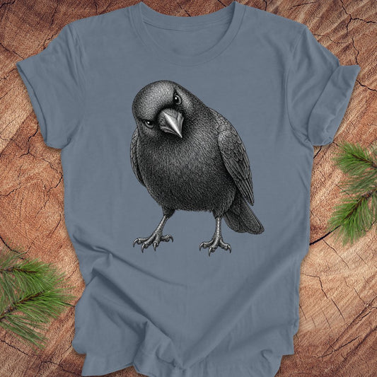 Steel blue t-shirt with a detailed pencil-style American Crow tilting its head and glaring, laid flat on a rustic wood background.