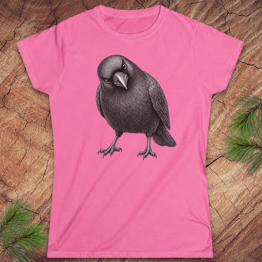Azalea pink women's t-shirt with a detailed pencil-style American Crow tilting its head and glaring, laid flat on a rustic wood background with pine branches.