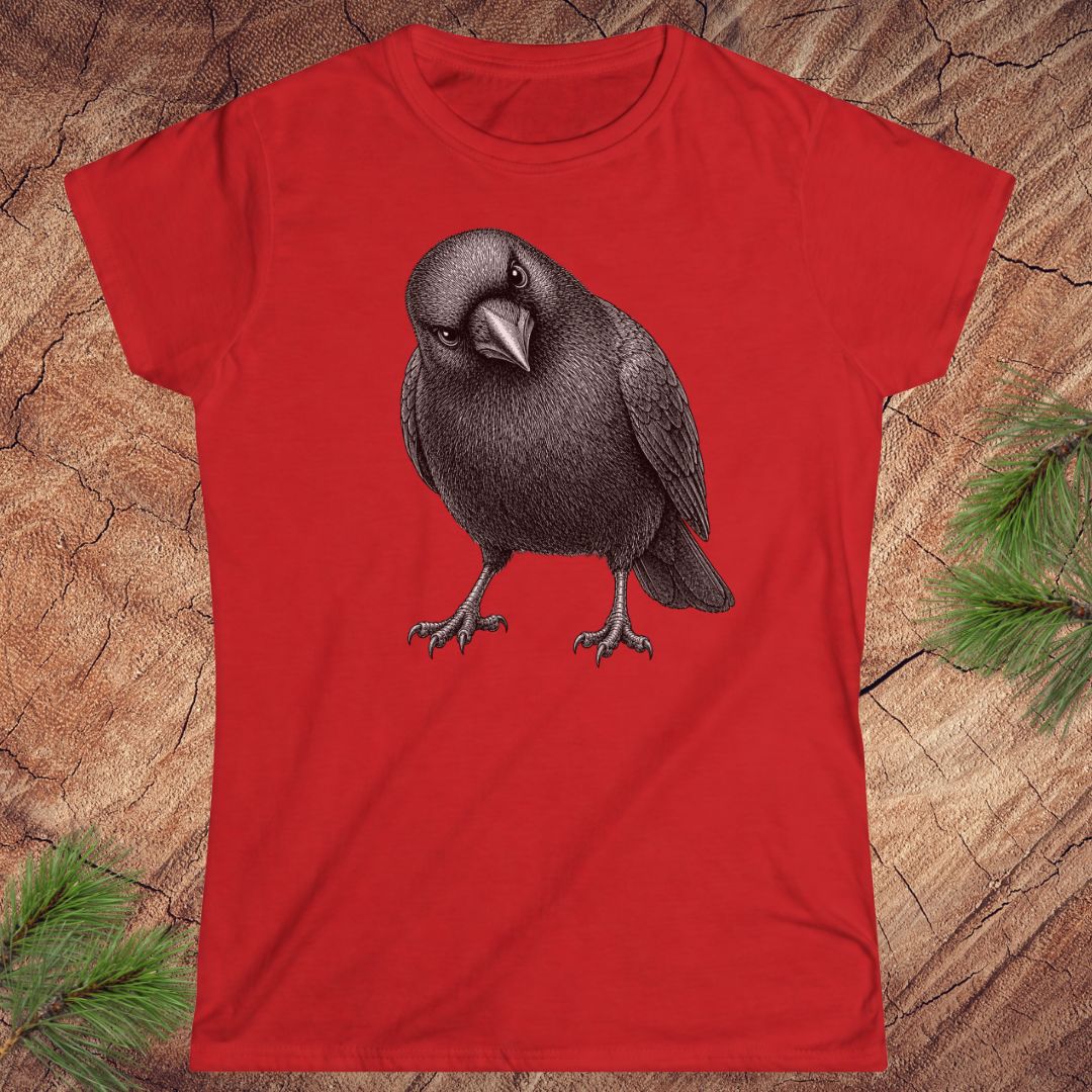 Red women's t-shirt with a detailed pencil-style American Crow tilting its head and glaring, laid flat on a rustic wood background with pine branches.