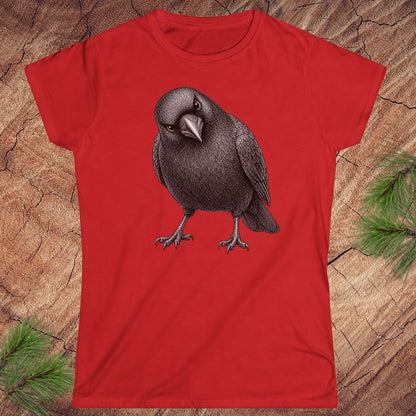 Red women's t-shirt with a detailed pencil-style American Crow tilting its head and glaring, laid flat on a rustic wood background with pine branches.