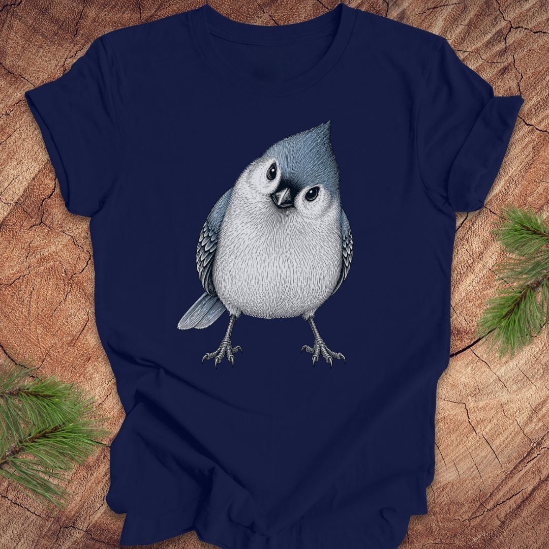 Navy blue t-shirt with a titmouse graphic on a wooden surface with pine branches.