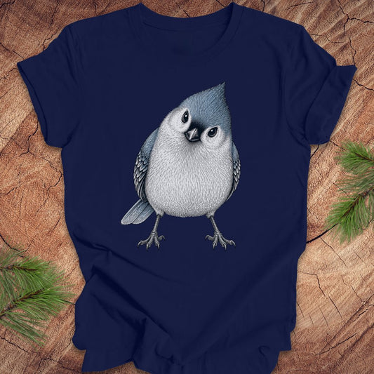 Navy blue t-shirt with a titmouse graphic on a wooden surface with pine branches.