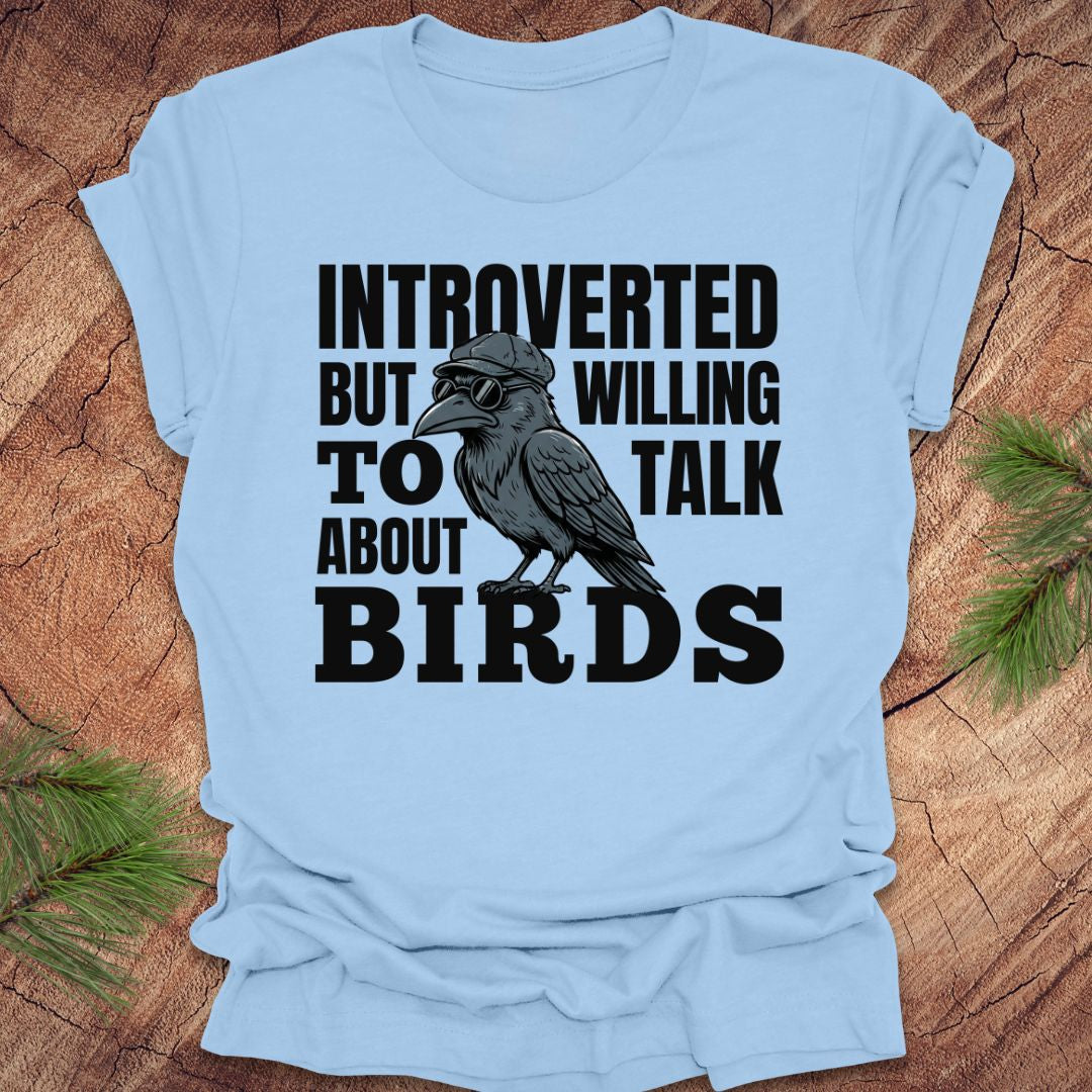 Light blue t-shirt with a graphic of a crow and text on a wooden surface.