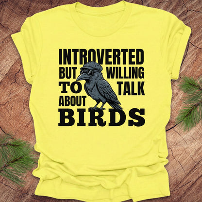 Yellow t-shirt with a black crow graphic and text on a wooden surface.