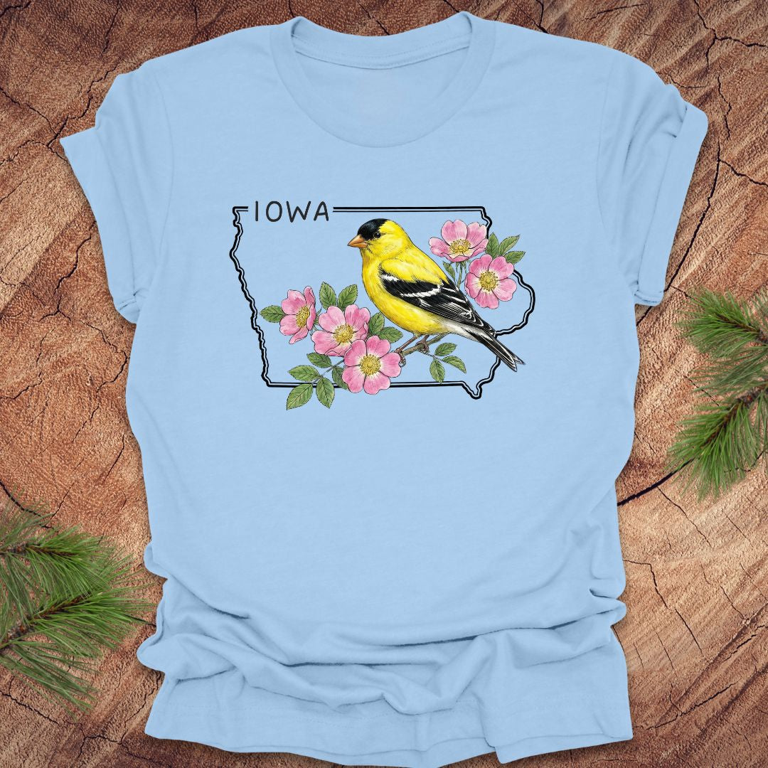Baby blue t-shirt with the outline of the state of Iowa with state bird and flower, goldfinch and rose, on a wood background.