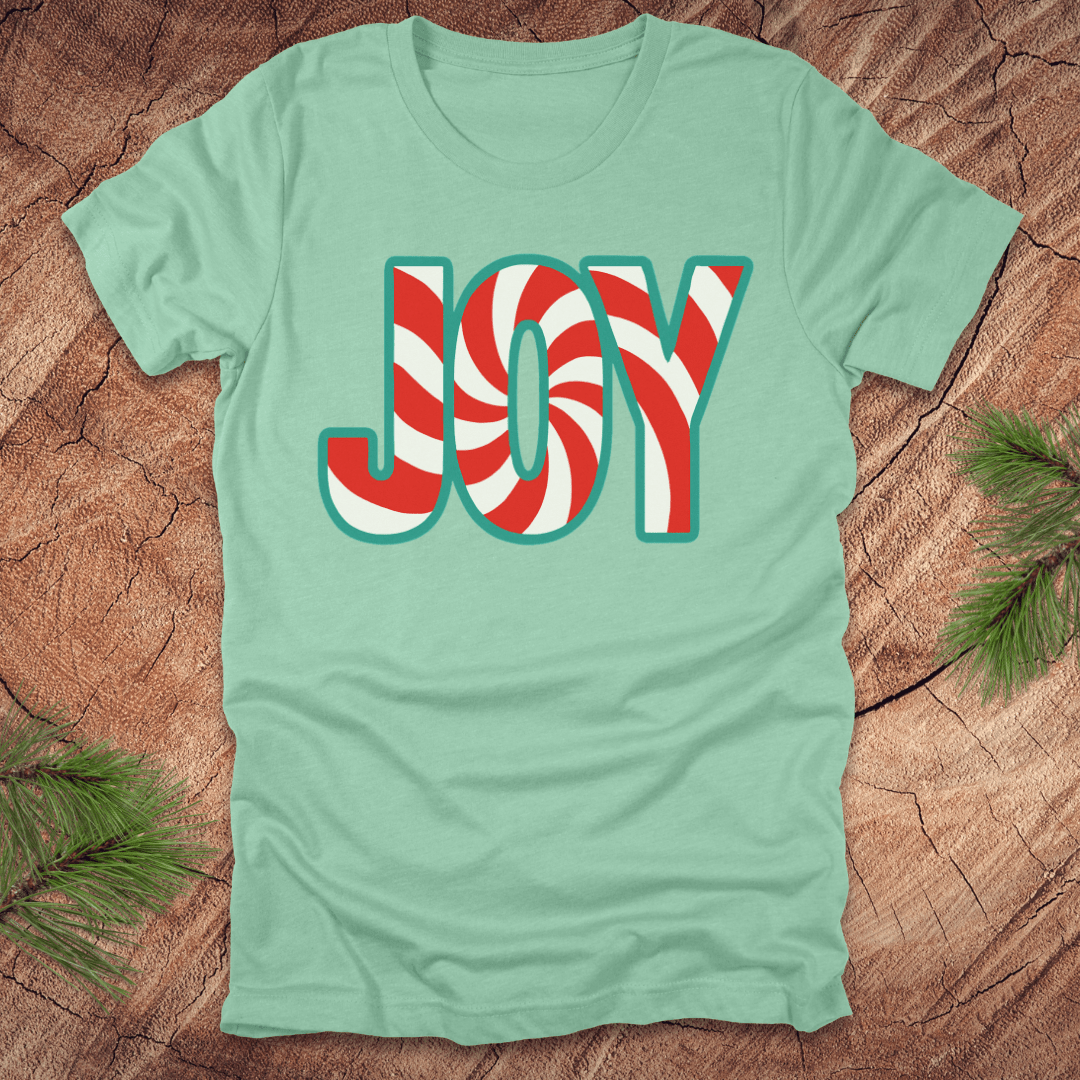 Mint green t-shirt with the text, "JOY" in a red and white pattern on a wood background