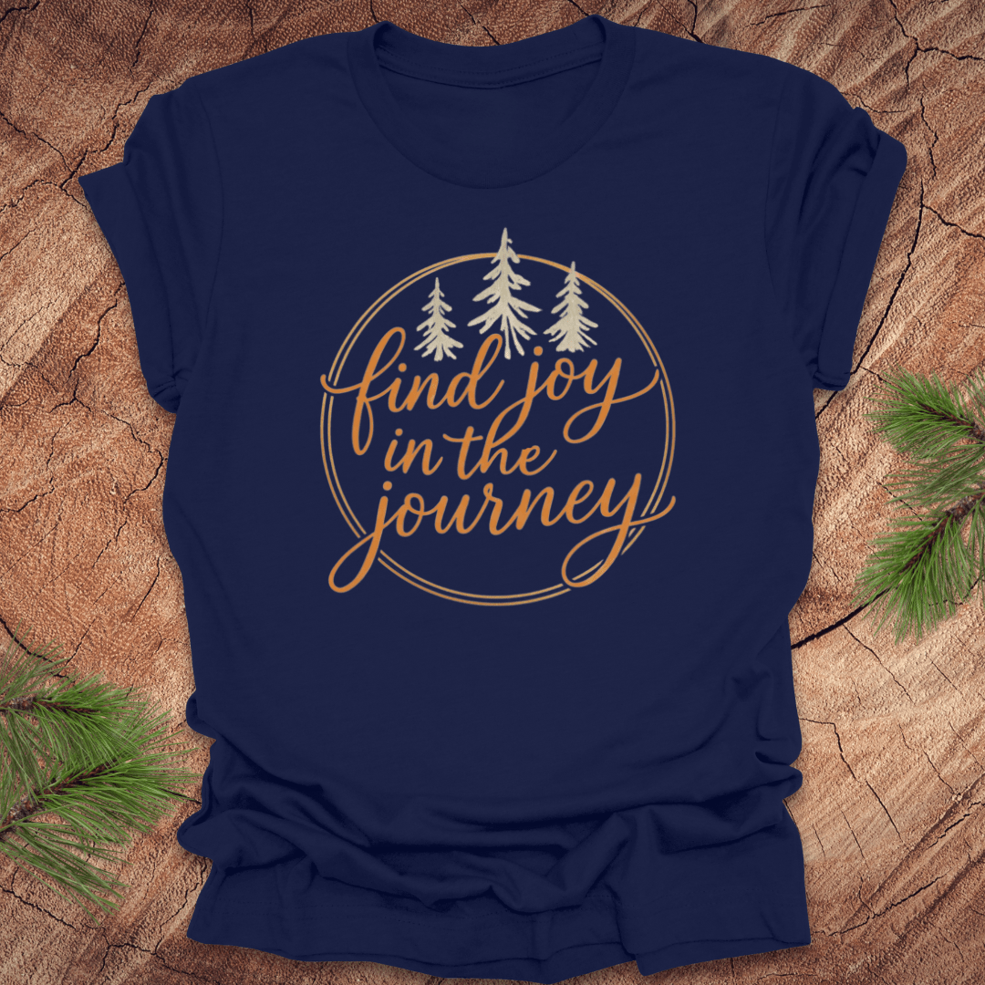 Navy blue t-shirt with 'find joy in the journey' text on a wooden surface with pine branches.