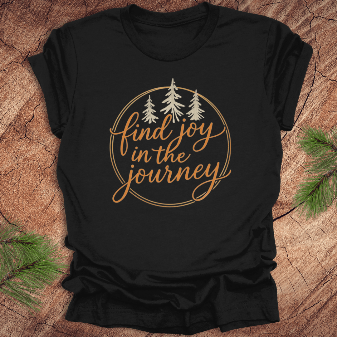 Black t-shirt with 'find joy in the journey' text and trees on a wooden surface.