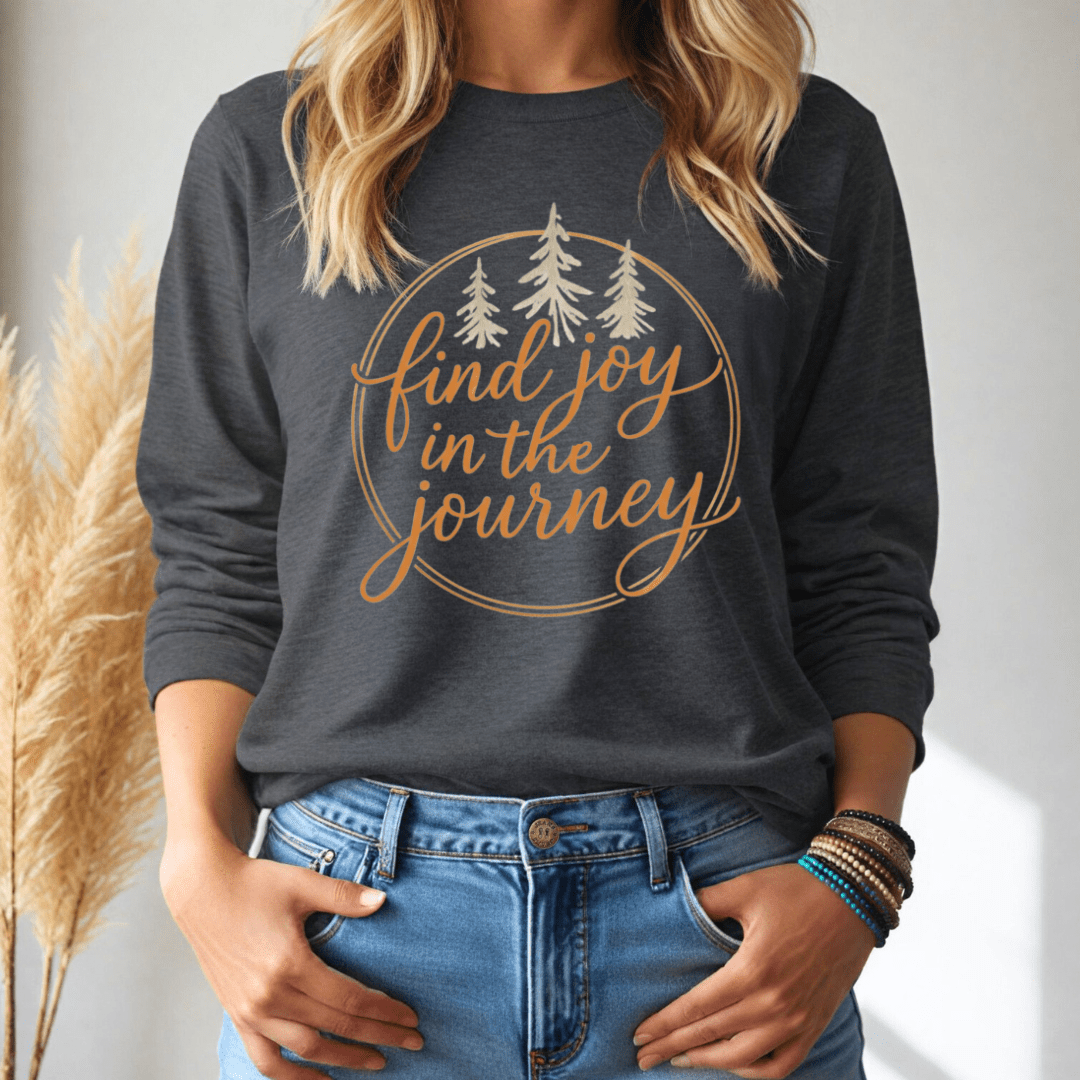 Person wearing a dark gray long-sleeve shirt with 'find joy in the journey' text and trees, standing against a neutral background.